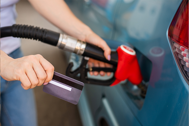 A woman fills her car with gasoline at a self-service gas station and holds a credit card
