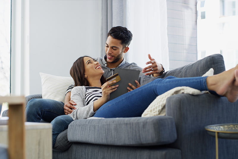 couple sitting on a couch. Woman with tablet and credit card in hand