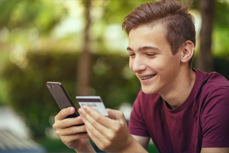 Teenage boy with a credit card and phone makes purchasing outdoors
